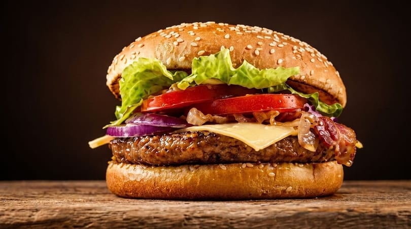 A juicy burger with lettuce, tomato, red onion, cheese, and bacon on a sesame seed bun.