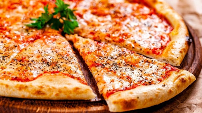 A whole cheese pizza with one slice removed, garnished with fresh parsley on a wooden board.