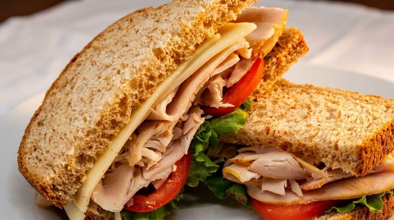 Two halves of a turkey and cheese sandwich on whole wheat bread with lettuce and tomato.